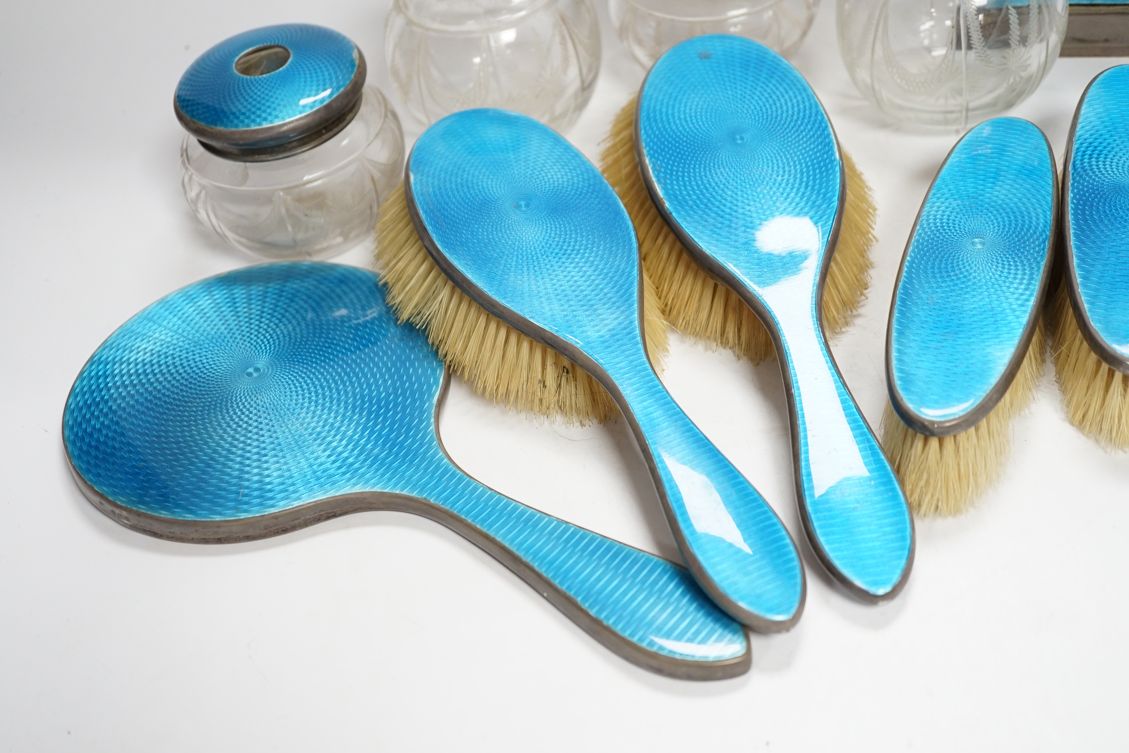 A George V silver and blue guilloche enamelled ten piece dressing table set, comprising four brushes, a hand mirror, two mounted glass toilet jars, two mounted glass scent and a mantel timepiece, 12.8cm, C.S Green & Co,
